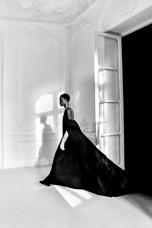 Платье из черного шифона с длинным шлейфом, модель грациозно движется по светлому помещению, создавая атмосферу загадки