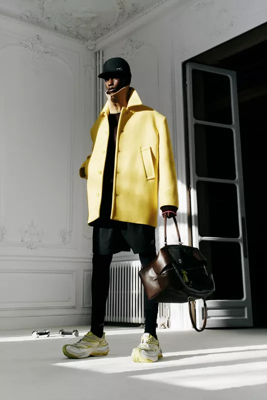 Яркий желтый пальто с крупными пуговицами, черные леггинсы и кроссовки, создающие спортивный контраст в интерьере.
