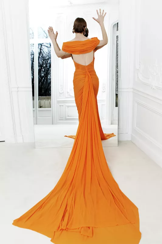 Яркое оранжевое платье с драпировкой и открытой спиной, подчеркивающее силуэт, на фоне белоснежного интерьера