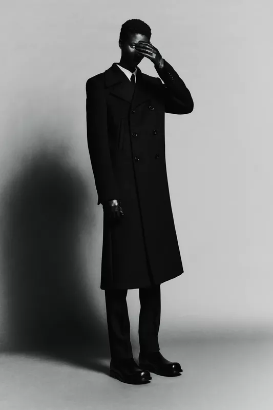 Строгий черный пальто с двойным рядом пуговиц, создающее эффектный контраст с серым фоном