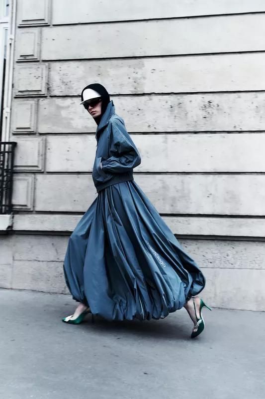 Объемный серый наряд с асимметричным силуэтом, дополненный зелеными туфлями и стильной кепкой, создает атмосферу уличной моды