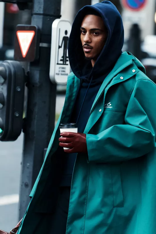Ярко-зеленый дождевик в сочетании с темным худи и стильными перчатками, создающий непринужденный городской образ