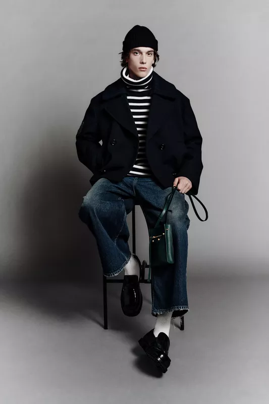 Стильный образ с черным двубортным пальто и полосатым свитером, дополненный широкими джинсами и зеленой сумкой