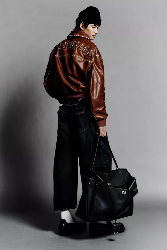 Кожаная куртка с заклепками и широкие джинсы, образ завершает черная сумка и стильная шапка, создавая дерзкий лук