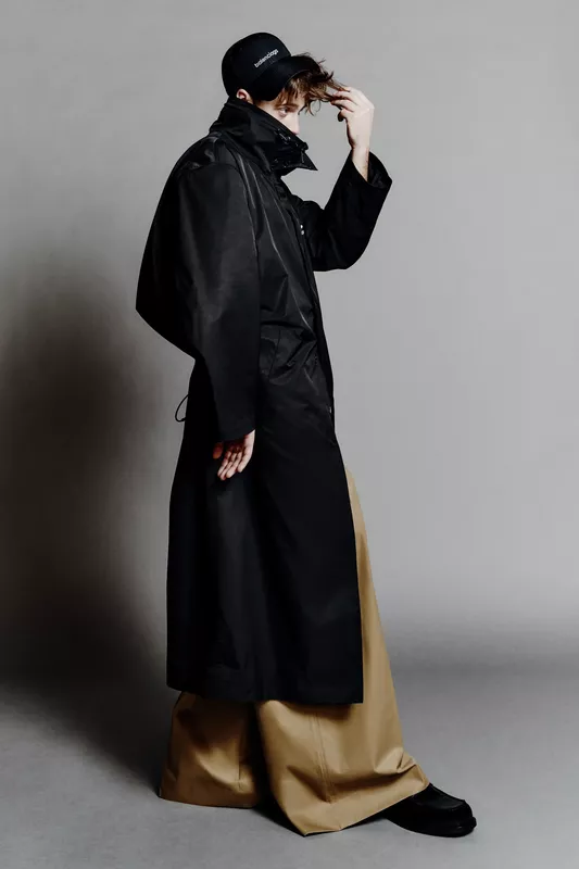Черный дождевик с широкими рукавами и светлыми брюками, подчеркивающий контрастные текстуры и силуэт