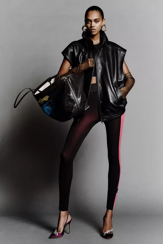 Объемный черный кожаный жилет в сочетании с облегающими леггинсами и яркими туфлями, создающими стильный контраст