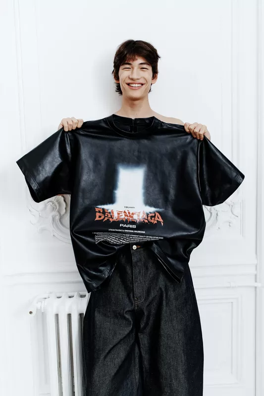 Улыбающийся молодой человек держит черную футболку с ярким принтом Balenciaga, подчеркивая креативный подход бренда