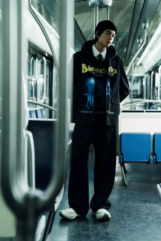 Ультрамодный черный костюм с ярким принтом и кроссовками, создающий контраст с современным интерьером метро