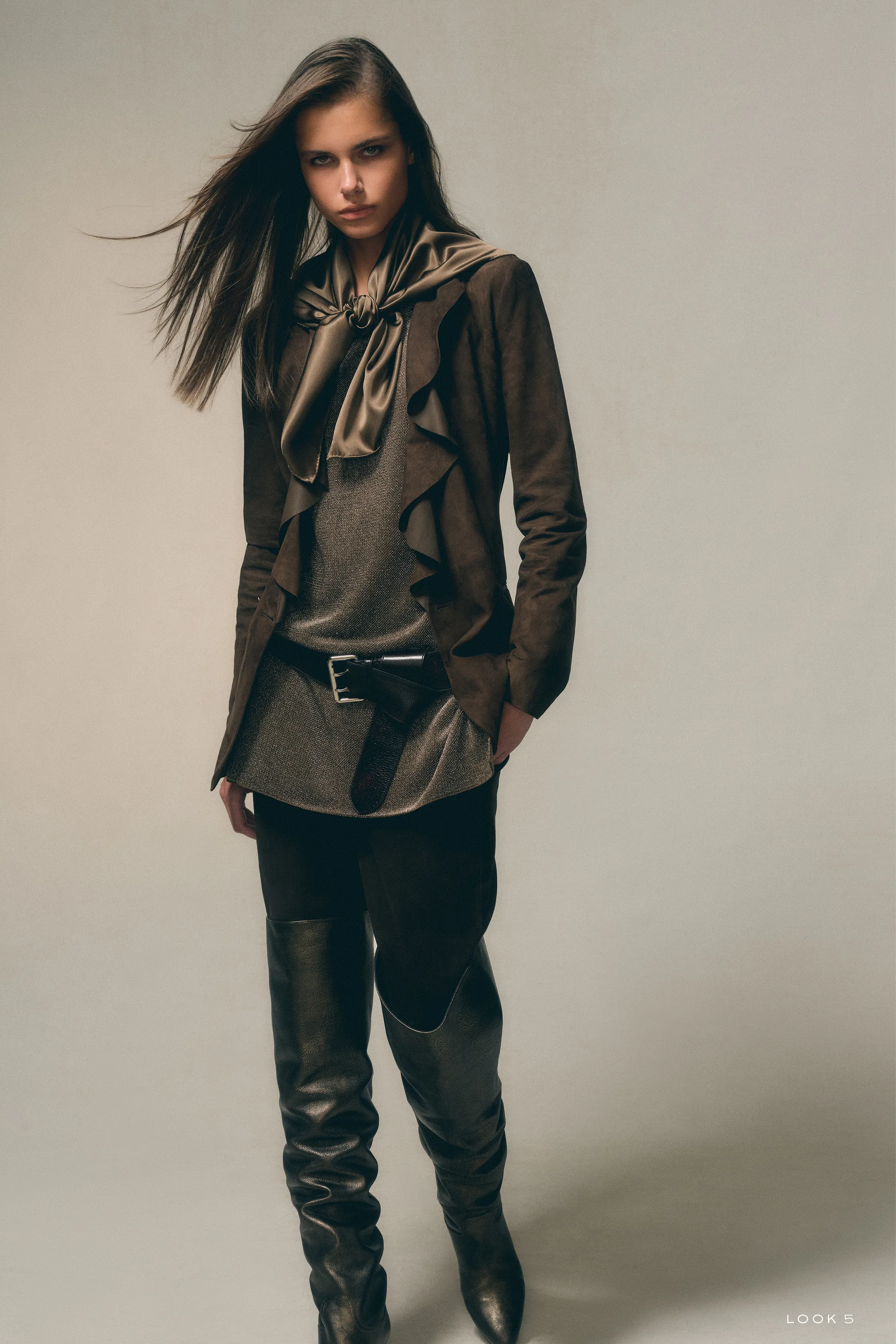 Модель в коричневом замшевом пиджаке с рюшами и высоких кожаных сапогах, создающих элегантный силуэт