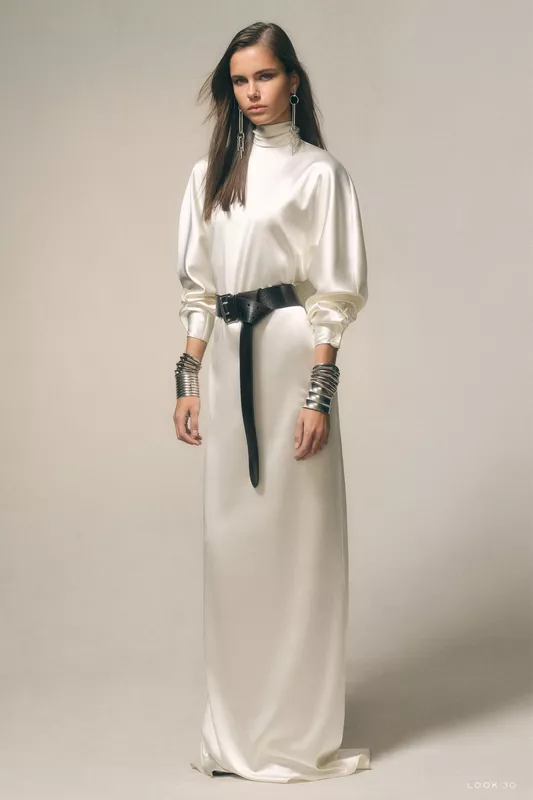 Элегантное белое платье с высоким воротником и кожаным поясом, дополненное металлическими браслетами, создает утонченный образ