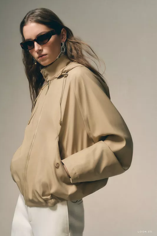 Нежный бежевый бомбер с капюшоном, дополненный стильными солнцезащитными очками и крупными серьгами, создаёт атмосферу уюта