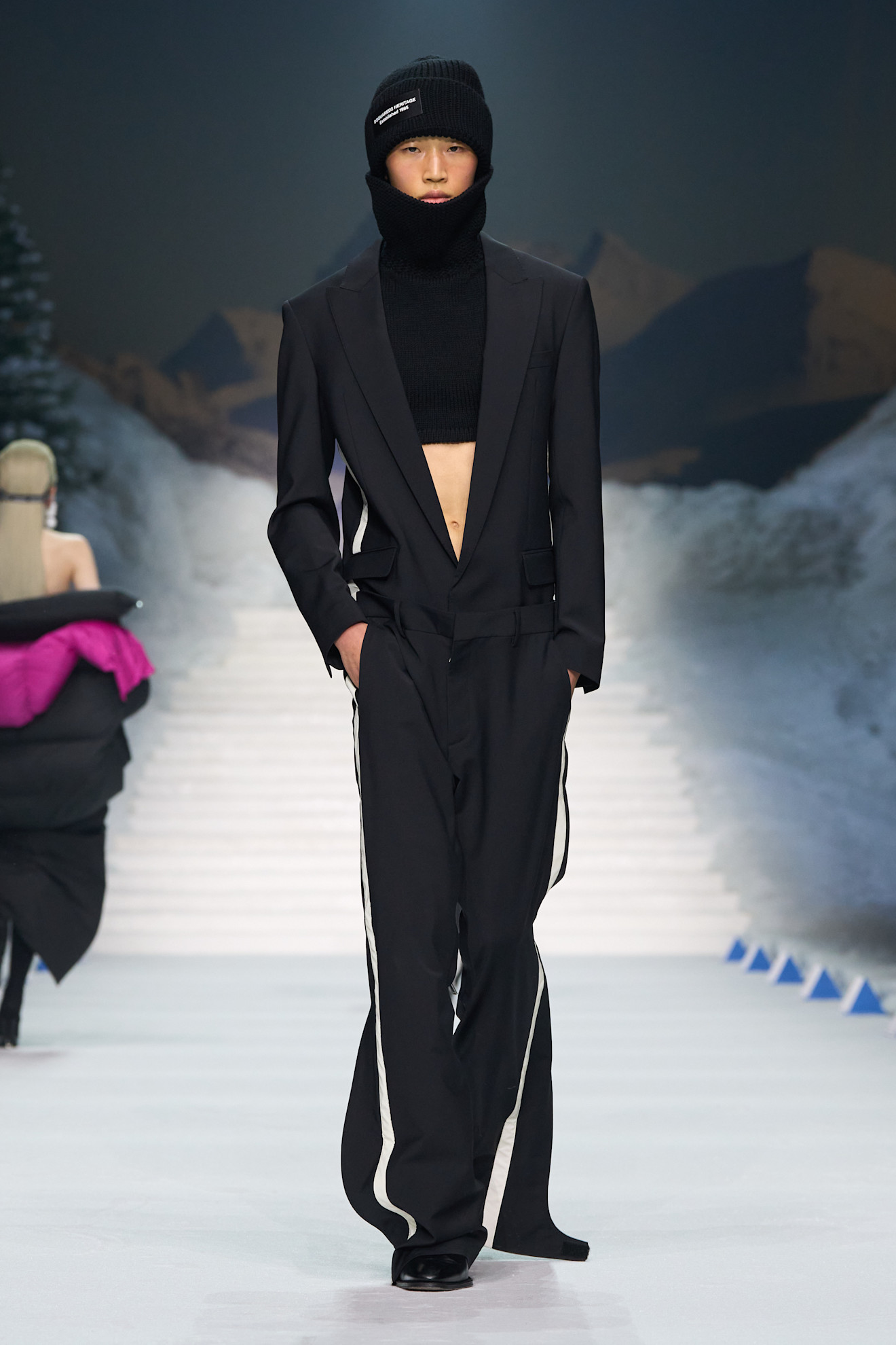 Элегантный черный костюм с укороченным свитером и шапкой, создающий контраст между формальным и спортивным стилем