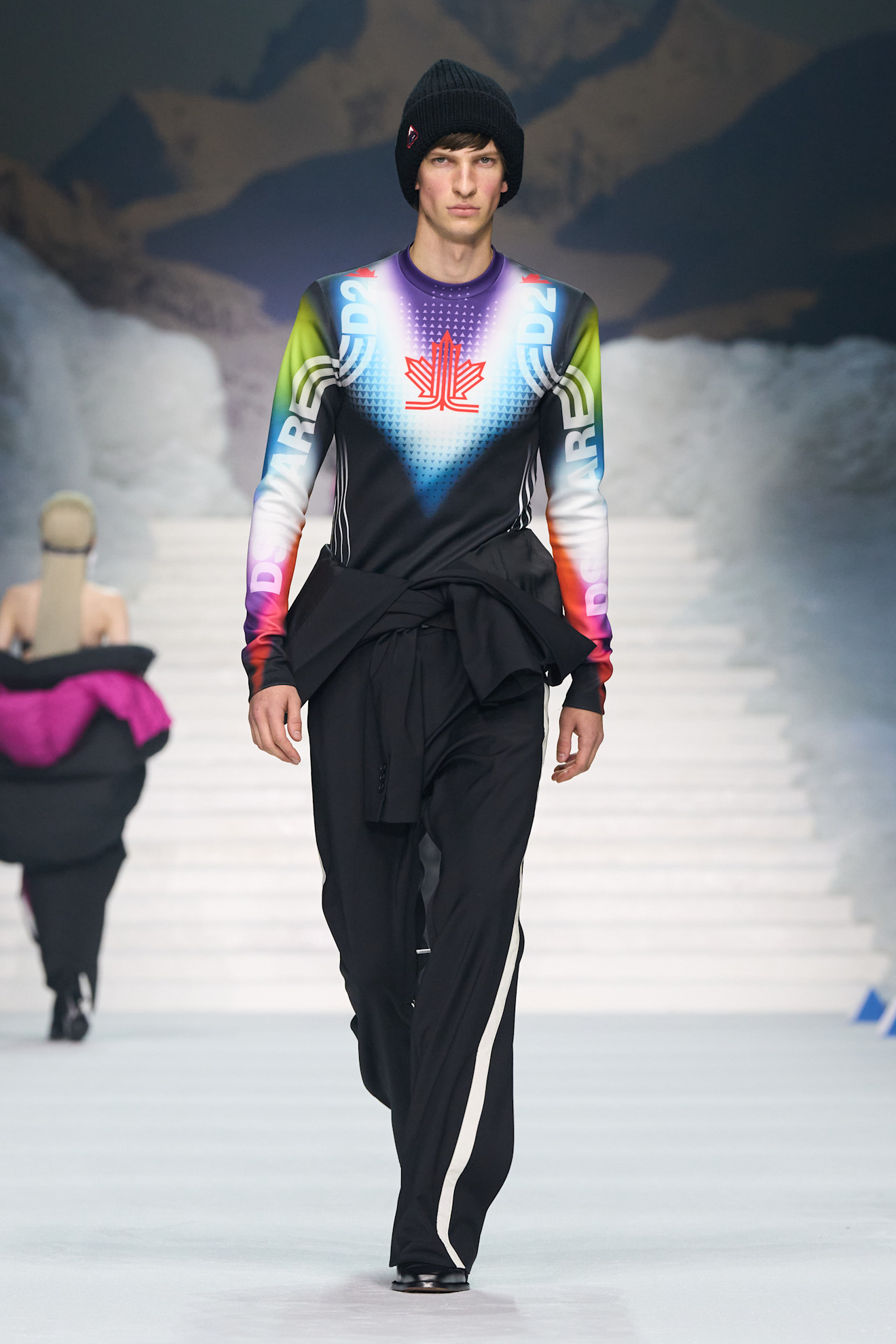 Яркий спортивный топ с графикой и черные брюки с белыми полосами, дополненные шапкой, создают стильный зимний образ