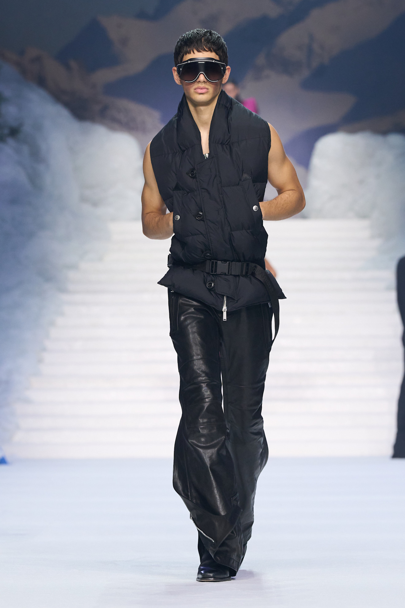 Черный жилет с пуховиками и кожаные брюки, дополненные массивными очками, подчеркивают мужественность и современный стиль