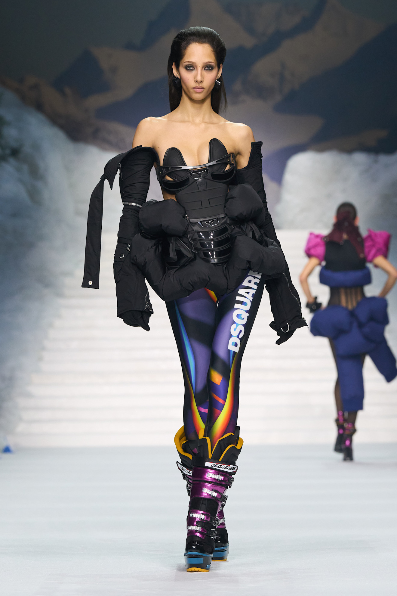 Модель в черном корсете и объемной куртке, дополненной яркими леггинсами и лыжными ботинками, создает смелый зимний look