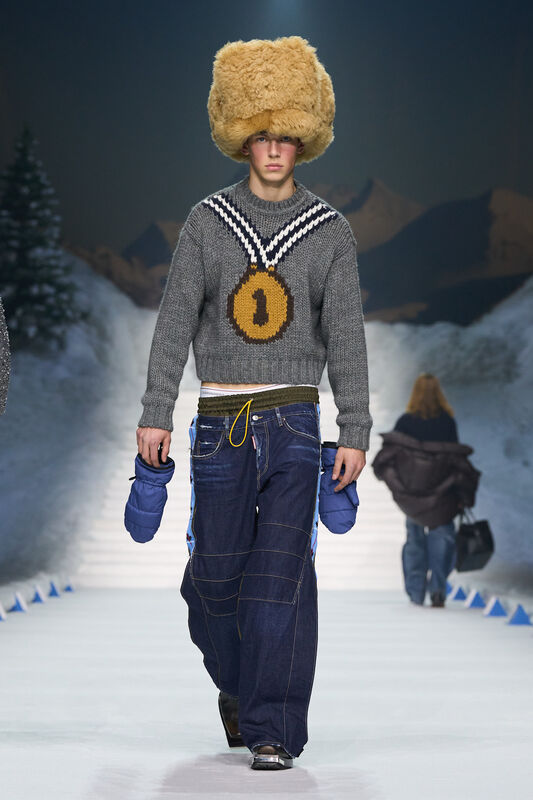 Объемная шапка из меха и свитер с медалью создают игривый зимний образ, дополненный широкими джинсами и перчатками.