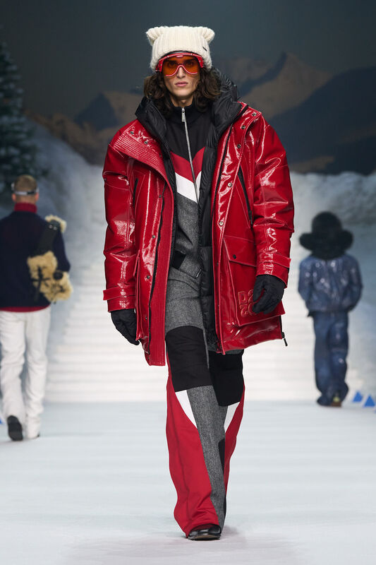 Яркий красный пуховик с блестящей текстурой, черные и серые брюки, дополненные шапкой с ушками и солнцезащитными очками