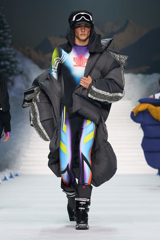 Объемный черный пуховик с блестящими деталями, яркий комбинезон с графикой, лыжные очки и шапка создают динамичный образ