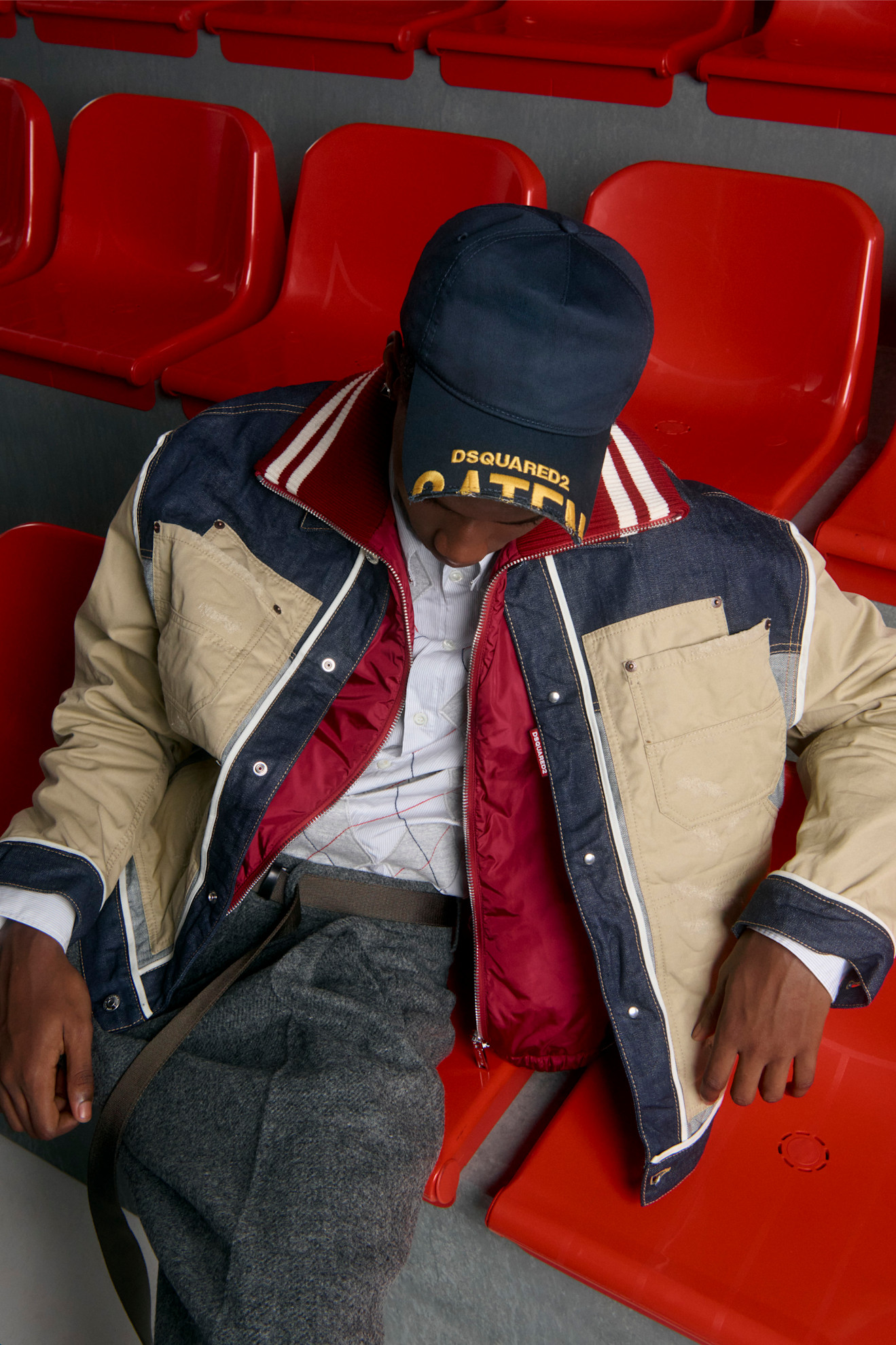 Расслабленный образ: двуцветная куртка с капюшоном и бейсболка, дополненные серыми брюками, на фоне красных сидений