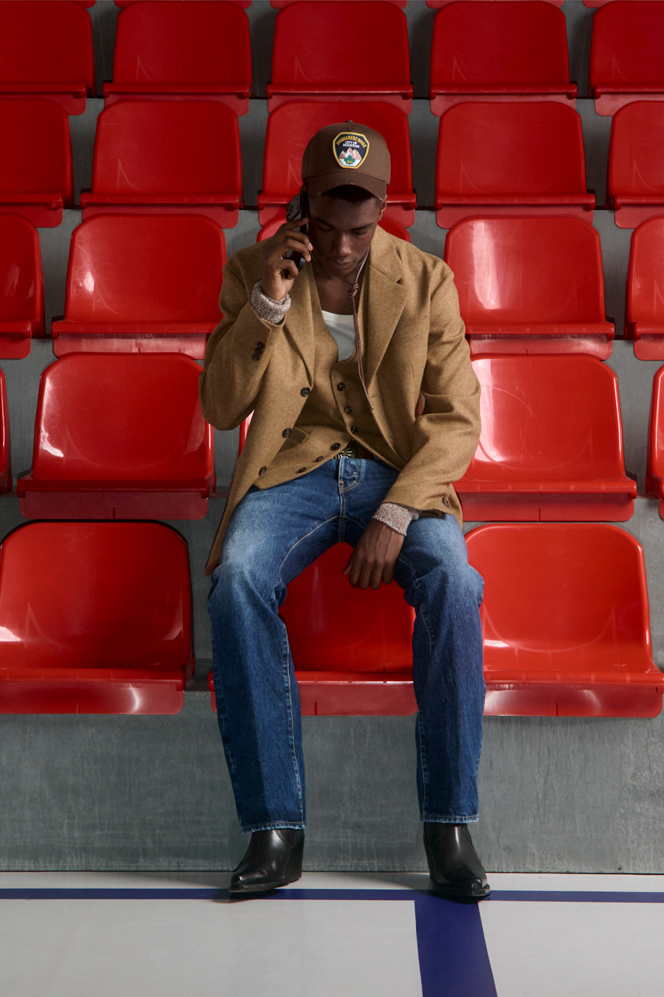 Классический бежевый пиджак в сочетании с джинсами и черными ботинками, создающий стильный городской образ на фоне красных сидений