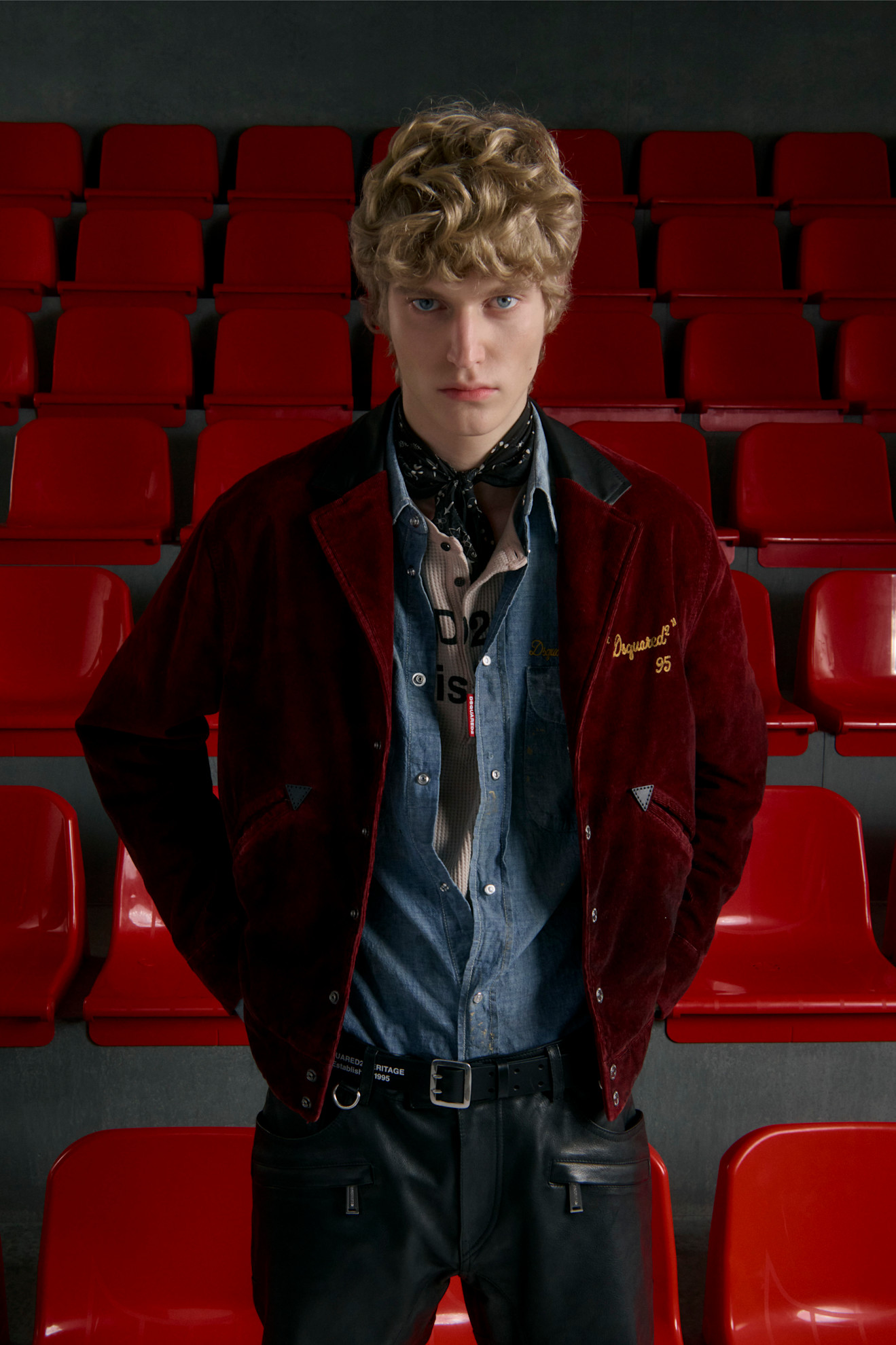 Вельветовая куртка бордового цвета с черной отделкой и джинсовой рубашкой, дополняет образ с шарфом и кожаными брюками