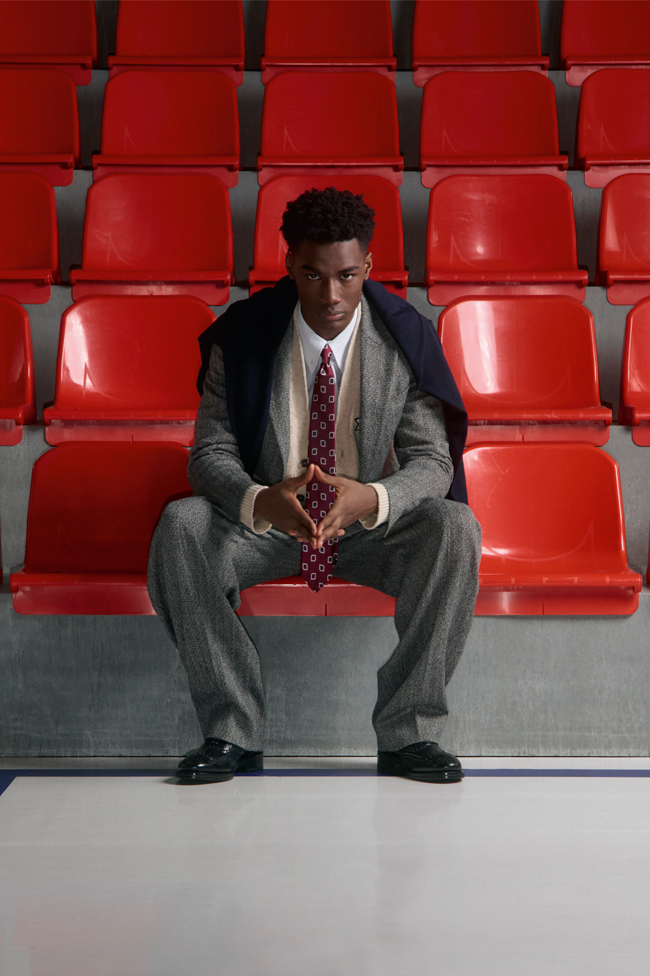 Строгий серый костюм с узором и красным галстуком, дополненный темным пиджаком, создает атмосферу уверенности