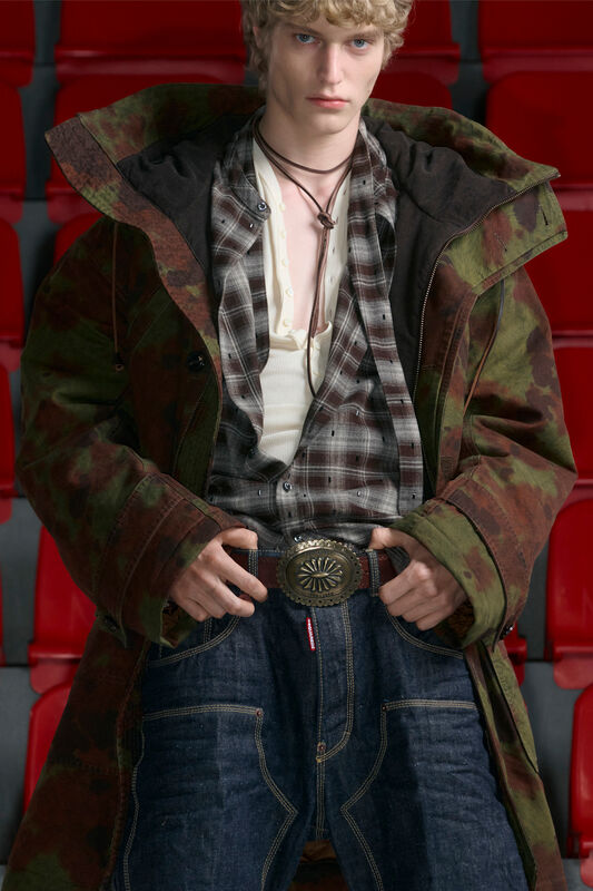 Молодой человек в камуфляжном пальто и клетчатой рубашке, с акцентом на стильный пояс и расслабленный вид