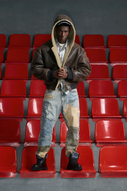 Модель в коричневой кожаной куртке с капюшоном и потертых джинсах, подчеркивающих неформальный стиль