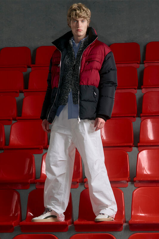 Стильный кэжуал: черно-красный пуховик, серый свитер и белые брюки, создающие яркий контраст с фоном