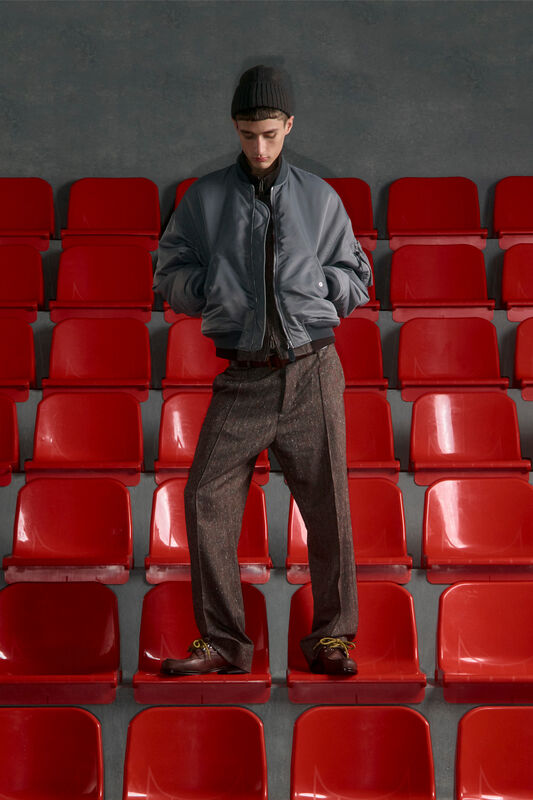 Серый бомбер и стильные брюки с текстурой, дополненные вязаной шапкой, на фоне ярких красных сидений