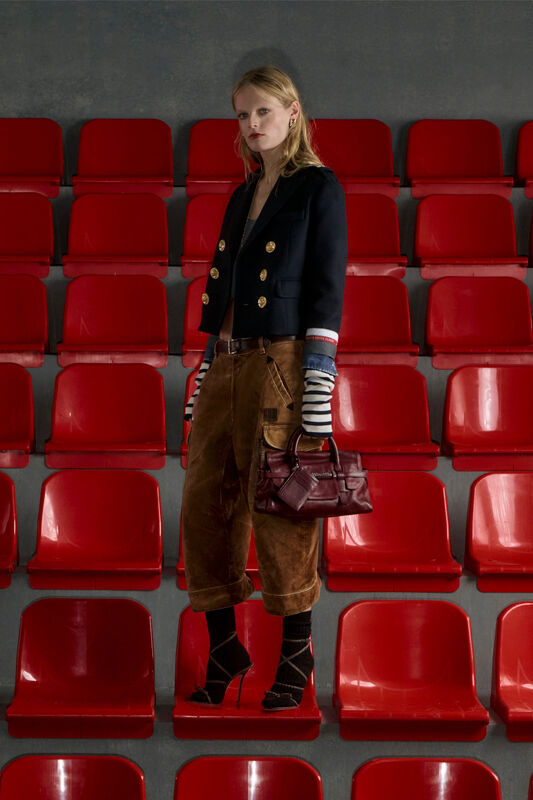 Темно-синий пиджак с золотыми пуговицами и коричневые вельветовые брюки, создающие стильный контраст с красными рядами