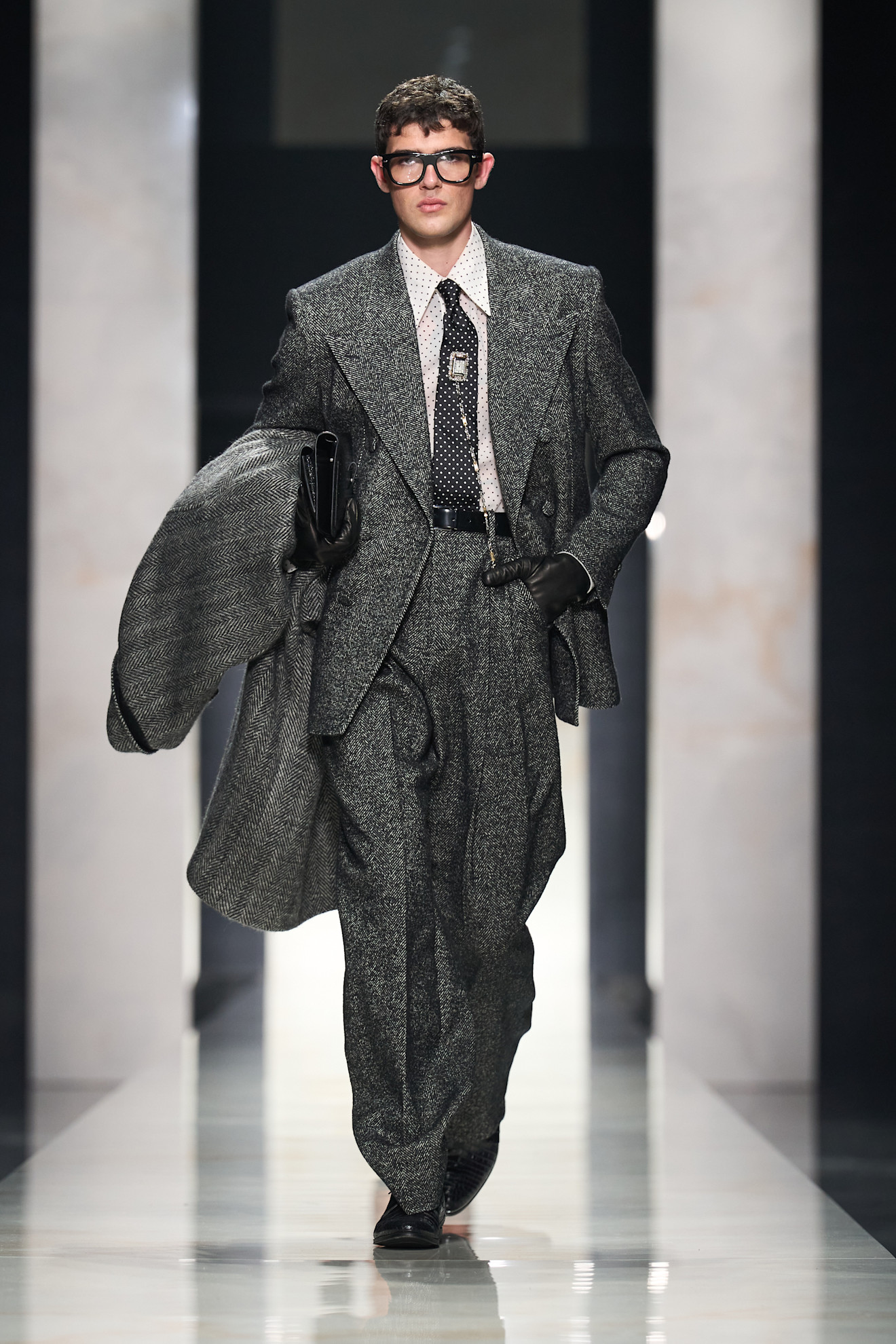 Элегантный серый костюм с крупной текстурой, дополненный черной галстуком и очками, вносит нотки ретро в современный образ