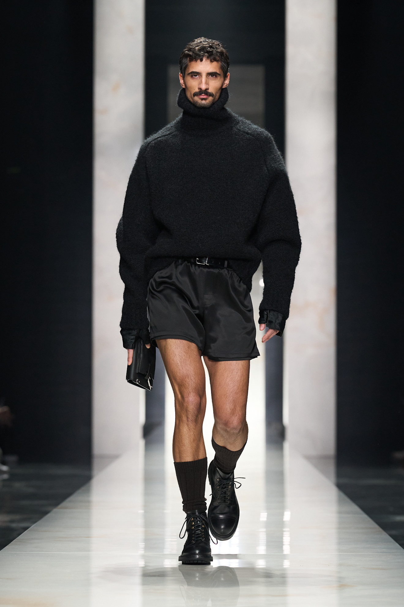 Контрастный черный свитер с высоким воротником и короткие шорты, завершенные ботинками, создают смелый и неожиданный стиль