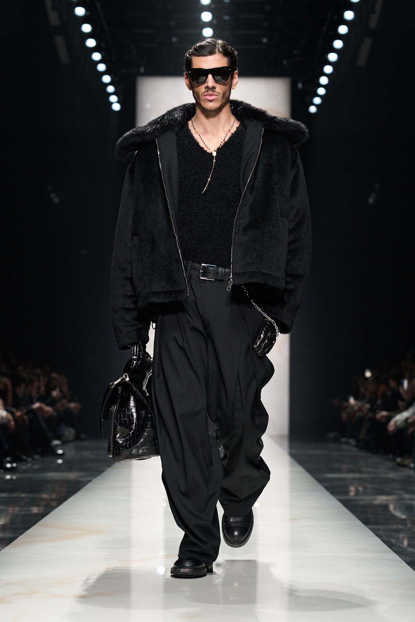 Элегантный образ с черной меховой курткой и широкими брюками, завершает стильные солнцезащитные очки и кожаная сумка