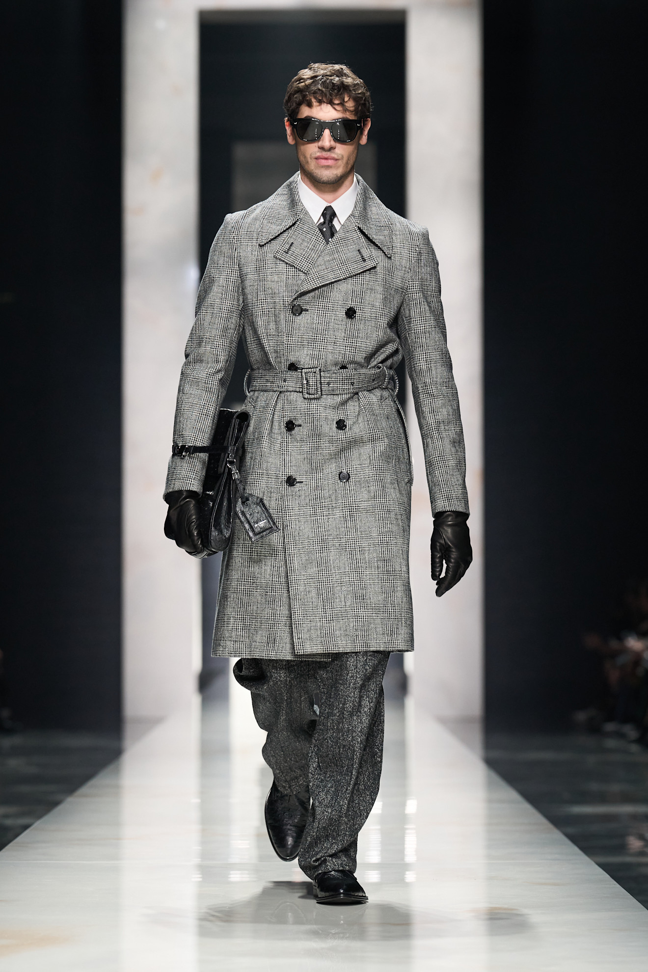 Модель в классическом сером пальто с двойной застежкой, дополненном черными очками и стильной сумкой, излучает уверенность