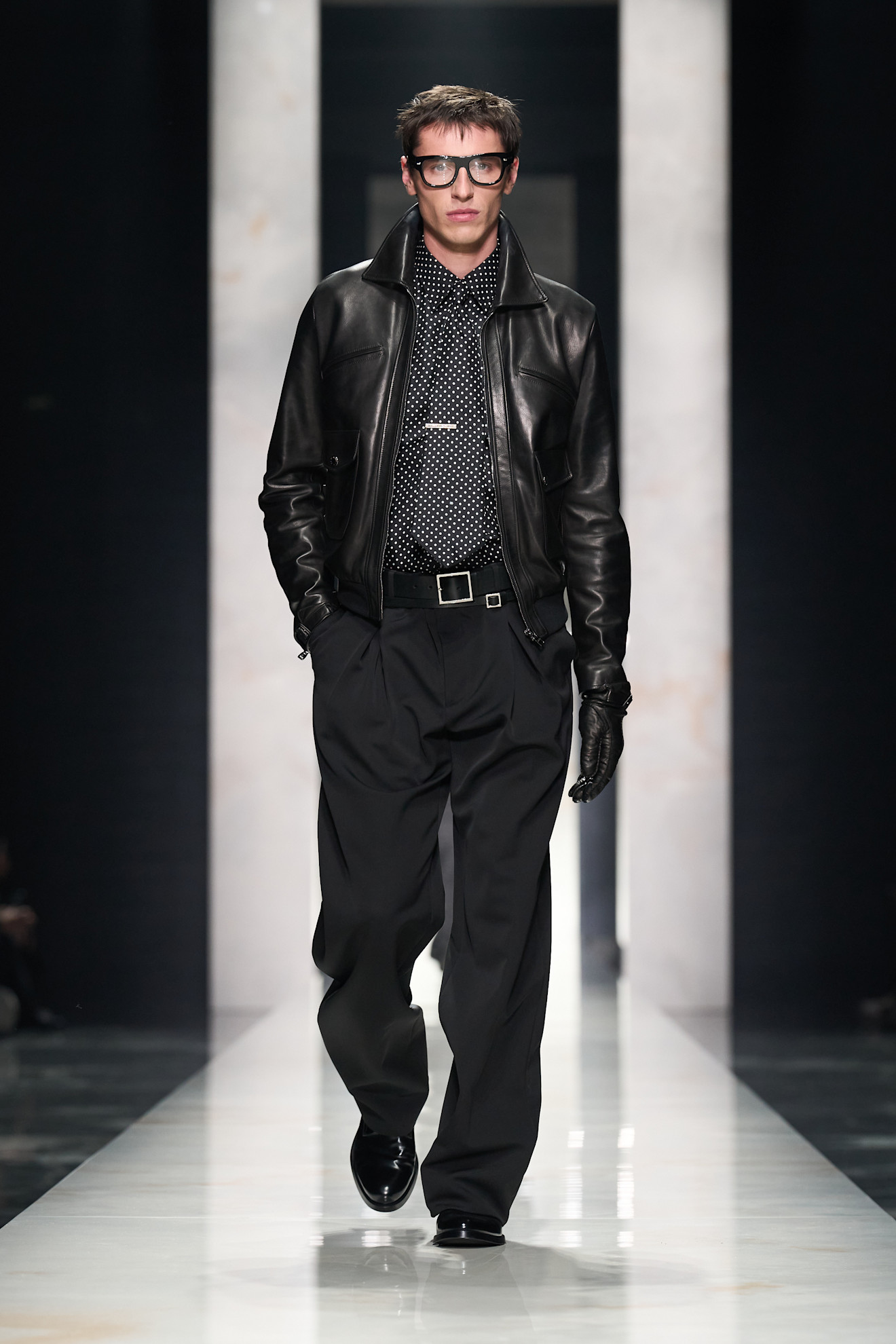 Кожаная куртка и рубашка в горошек создают смелый образ, дополненный широкими брюками и крупными очками, подчеркивающими индивидуальность