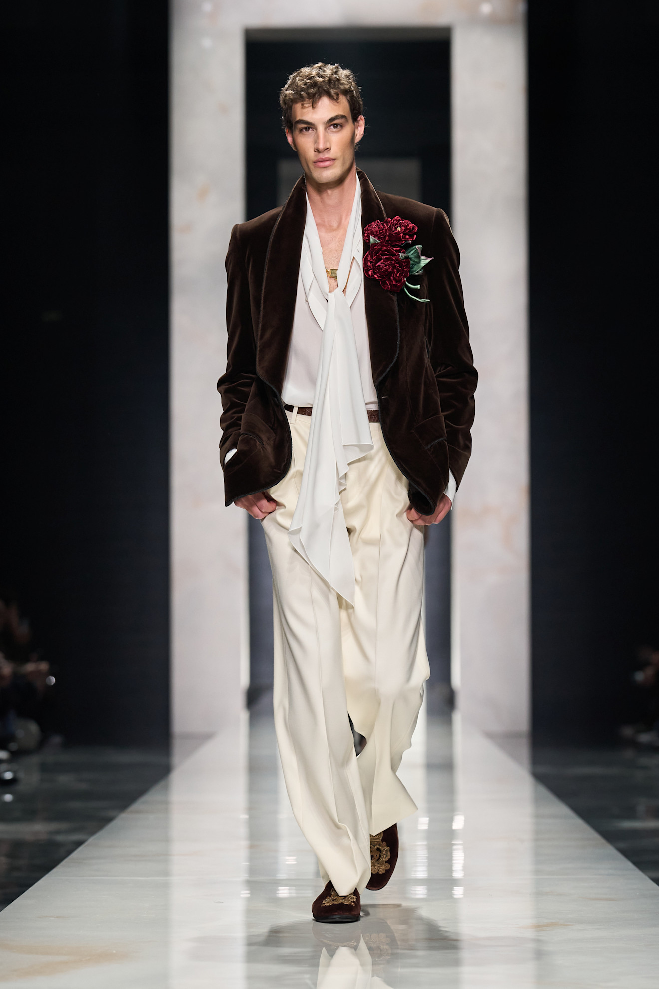 Модель в бархатном пиджаке с цветком на груди, светлой рубашке и светлых брюках, создаёт атмосферу утончённой роскоши