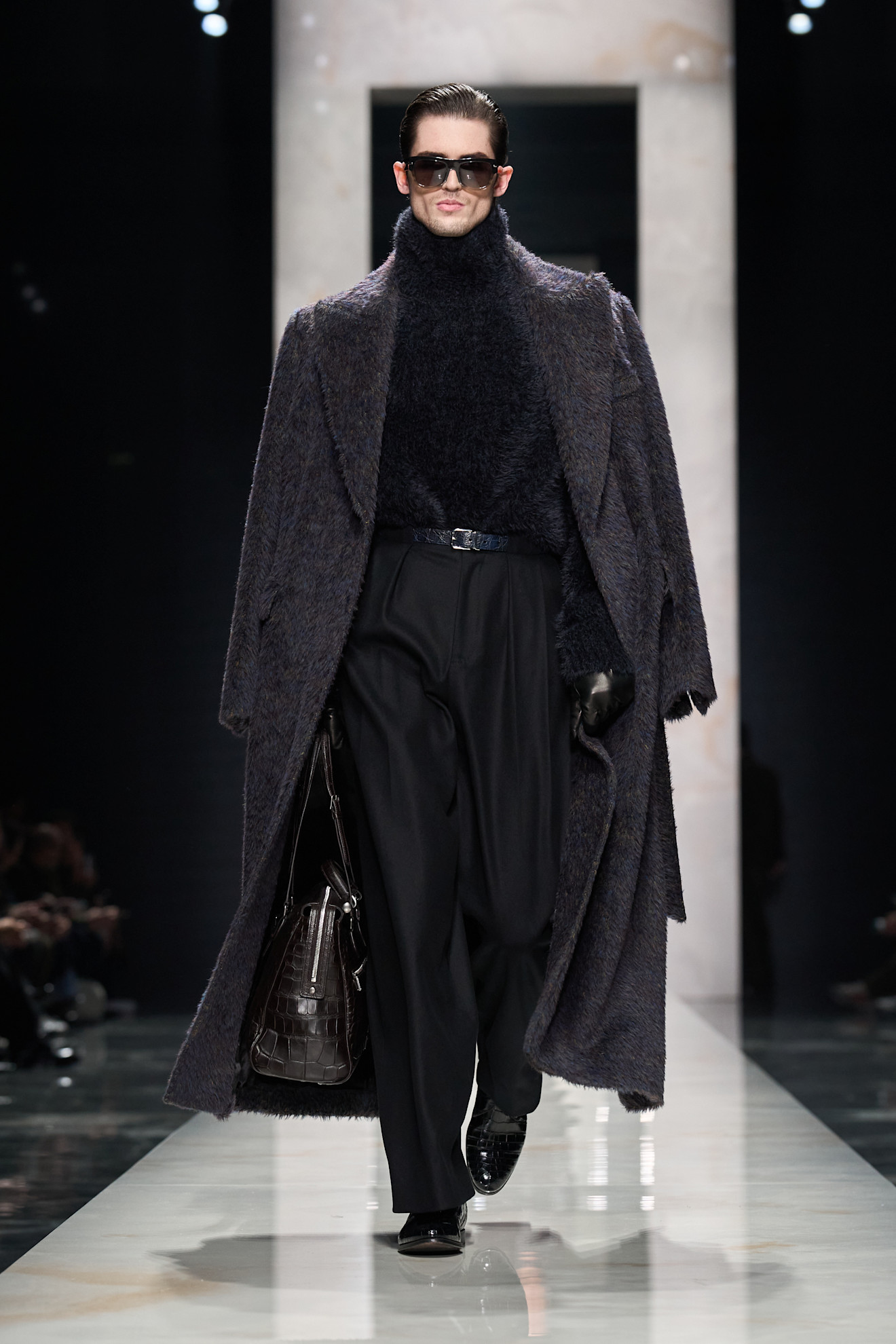 Модель в объемном темно-сером пальто и высоком воротнике, сочетает текстуры и стиль с элегантной сумкой и очками