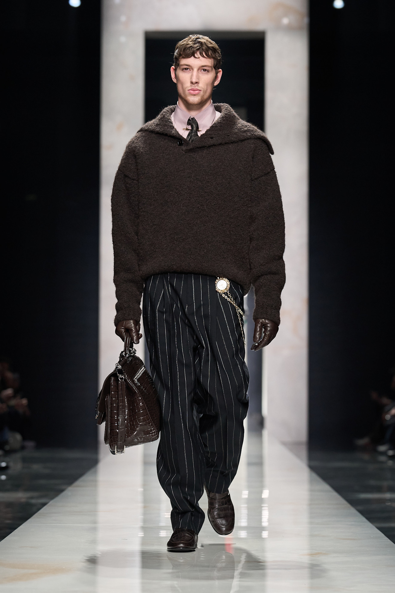 Модель в тёмно-коричневом свитере и полосатых брюках, дополненных стильной сумкой, создаёт атмосферу современного шика