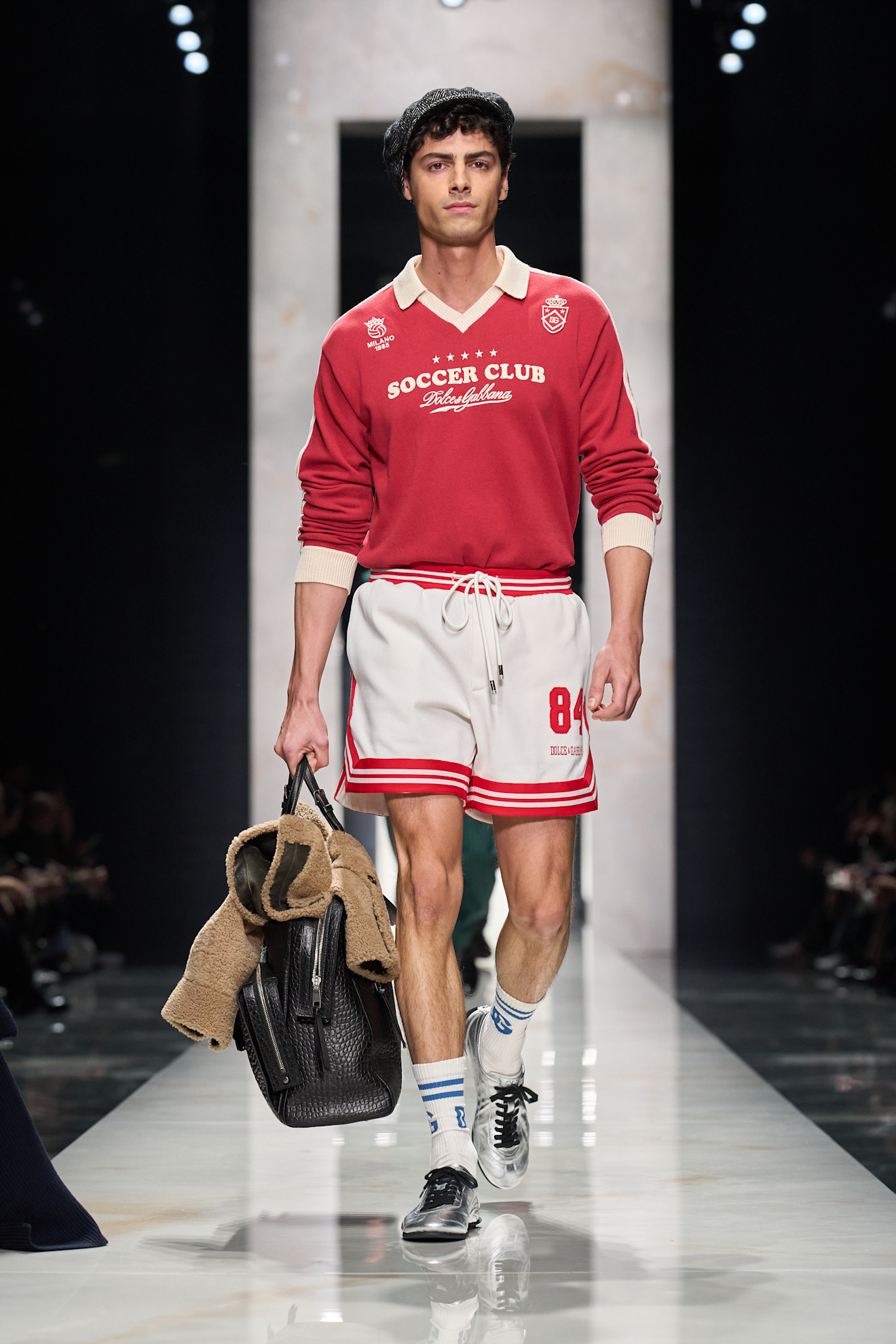 Красный свитер с логотипом и белые шорты с полосками, дополненные черной сумкой, придают спортивный шарм