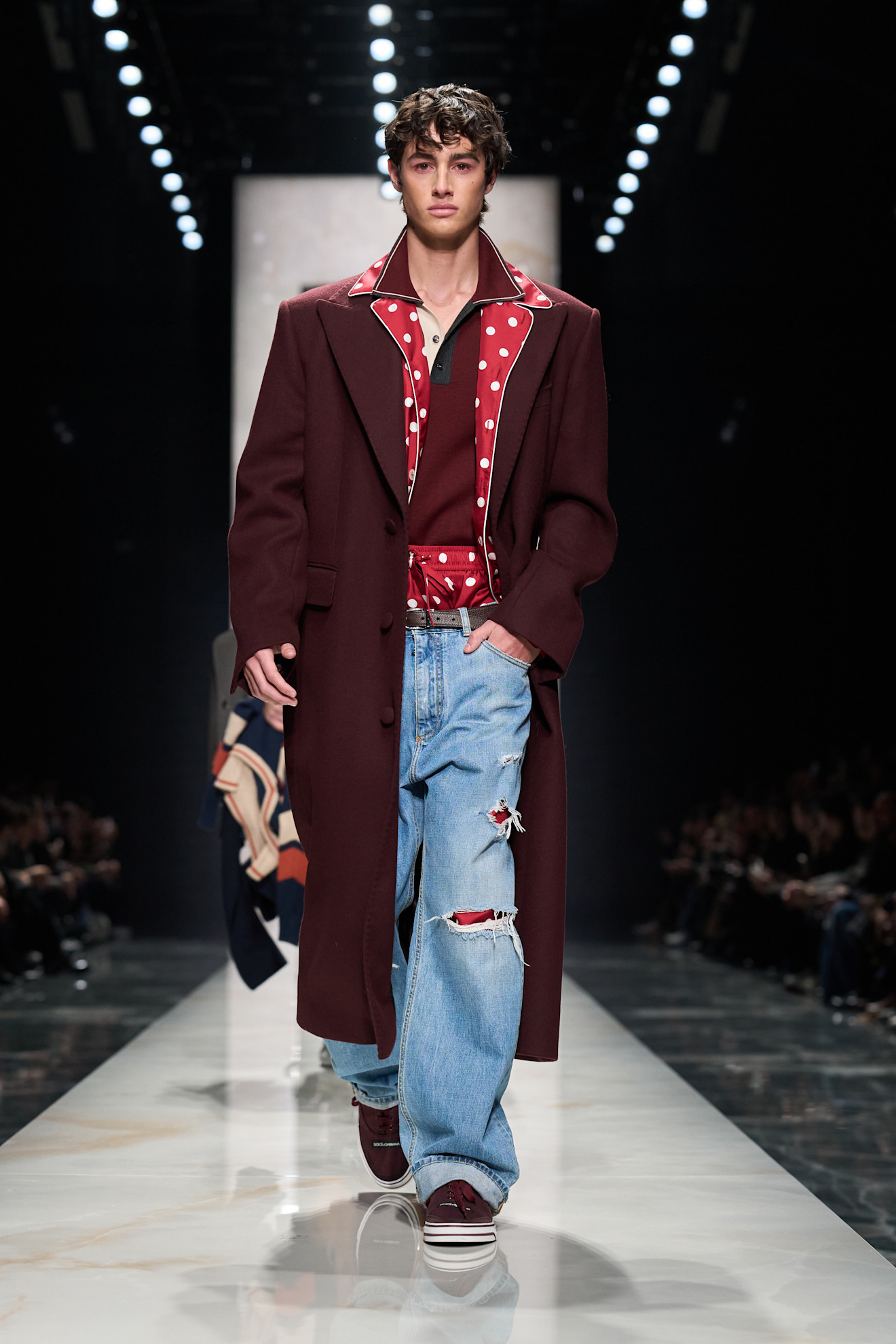 Модель в бордовом пальто с крупными пуговицами и рваными джинсами, создающая стильный контраст с яркой рубашкой в горошек