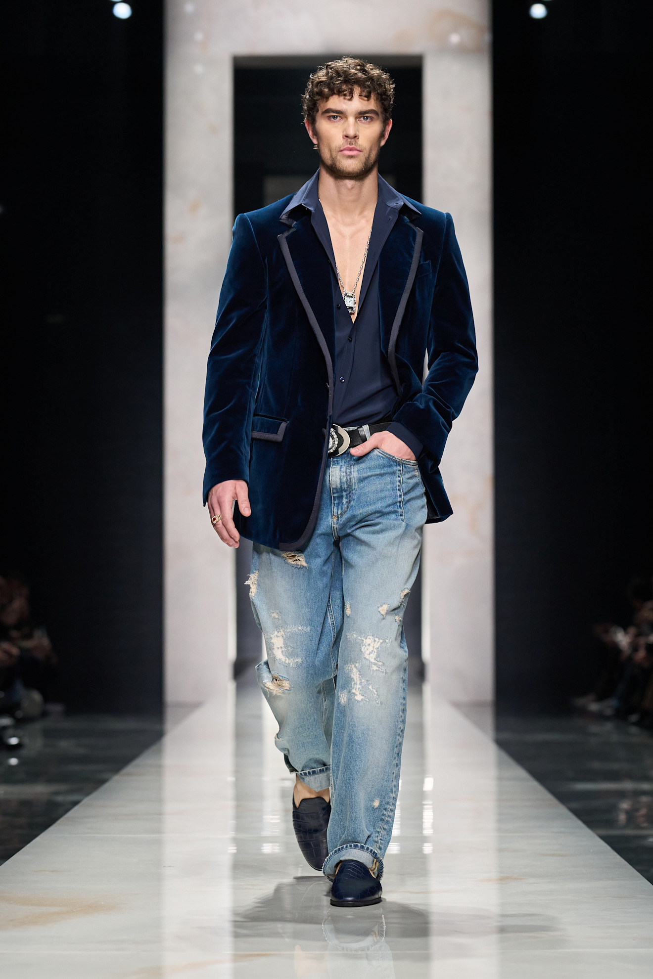 Модель в бархатном синем пиджаке и рваных джинсах, создающая стильный контраст между элегантностью и повседневностью