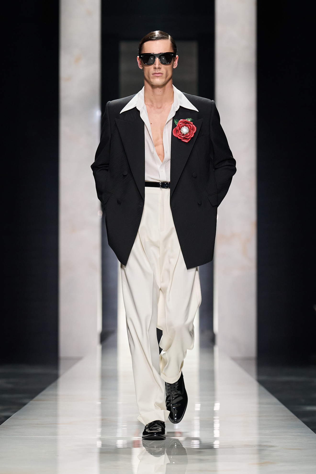 Черный пиджак с яркой красной розой и белыми брюками, создающий контрастный и смелый образ для модного показа