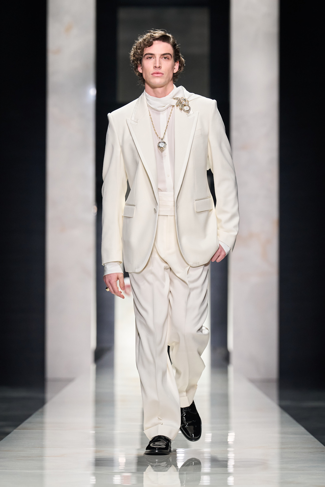 Светлый костюм с изысканными деталями, включая брошку и цепочку, создает атмосферу классической элегантности