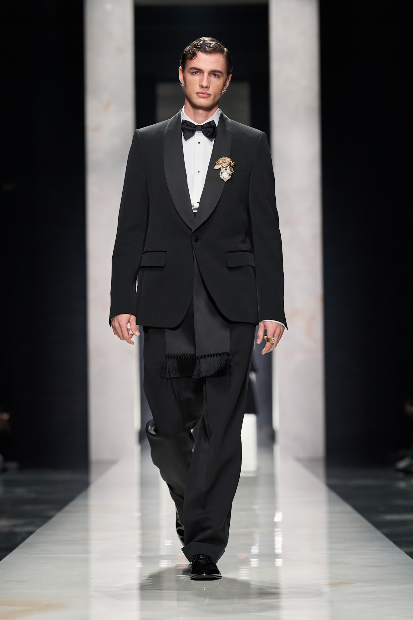 Классический черный смокинг с бабочкой и изысканной брошей, создающий атмосферу утонченности на подиуме