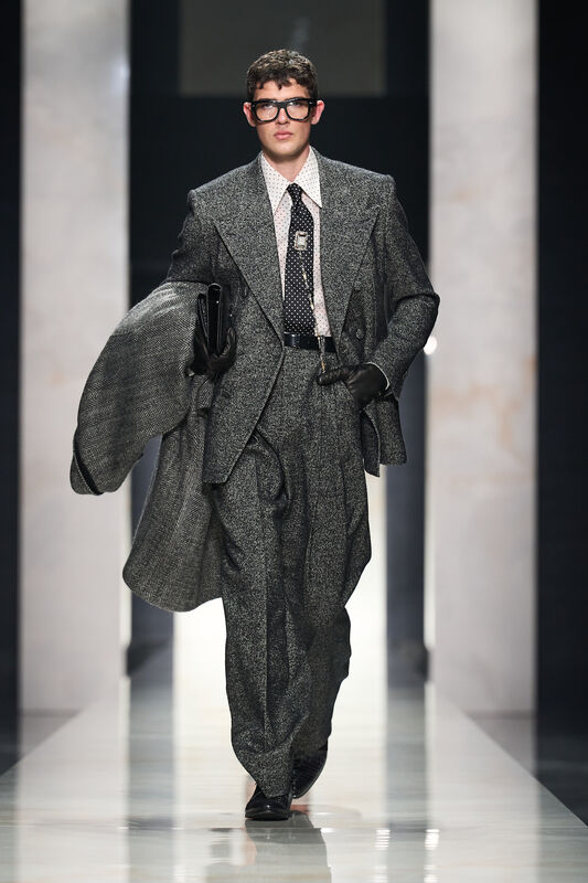 Элегантный серый костюм с крупной текстурой, дополненный черной галстуком и очками, вносит нотки ретро в современный образ