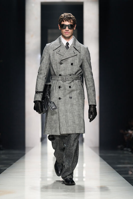 Модель в классическом сером пальто с двойной застежкой, дополненном черными очками и стильной сумкой, излучает уверенность