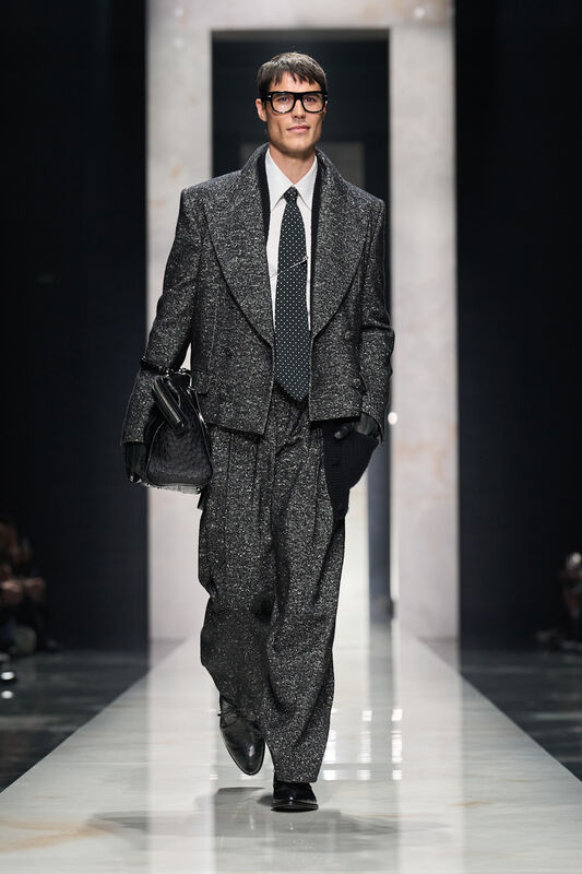 Стильный образ в блестящем сером костюме с объемными плечами и черным галстуком в горошек, создающий эффект уверенности