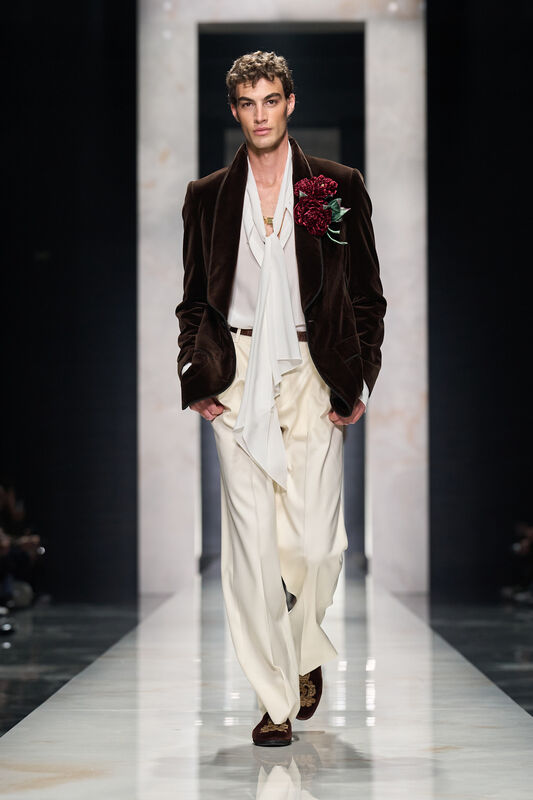 Модель в бархатном пиджаке с цветком на груди, светлой рубашке и светлых брюках, создаёт атмосферу утончённой роскоши