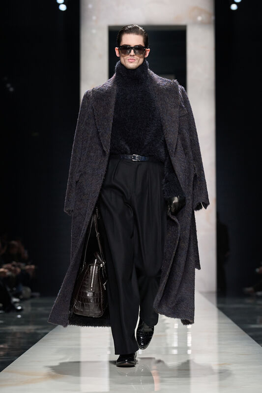 Модель в объемном темно-сером пальто и высоком воротнике, сочетает текстуры и стиль с элегантной сумкой и очками